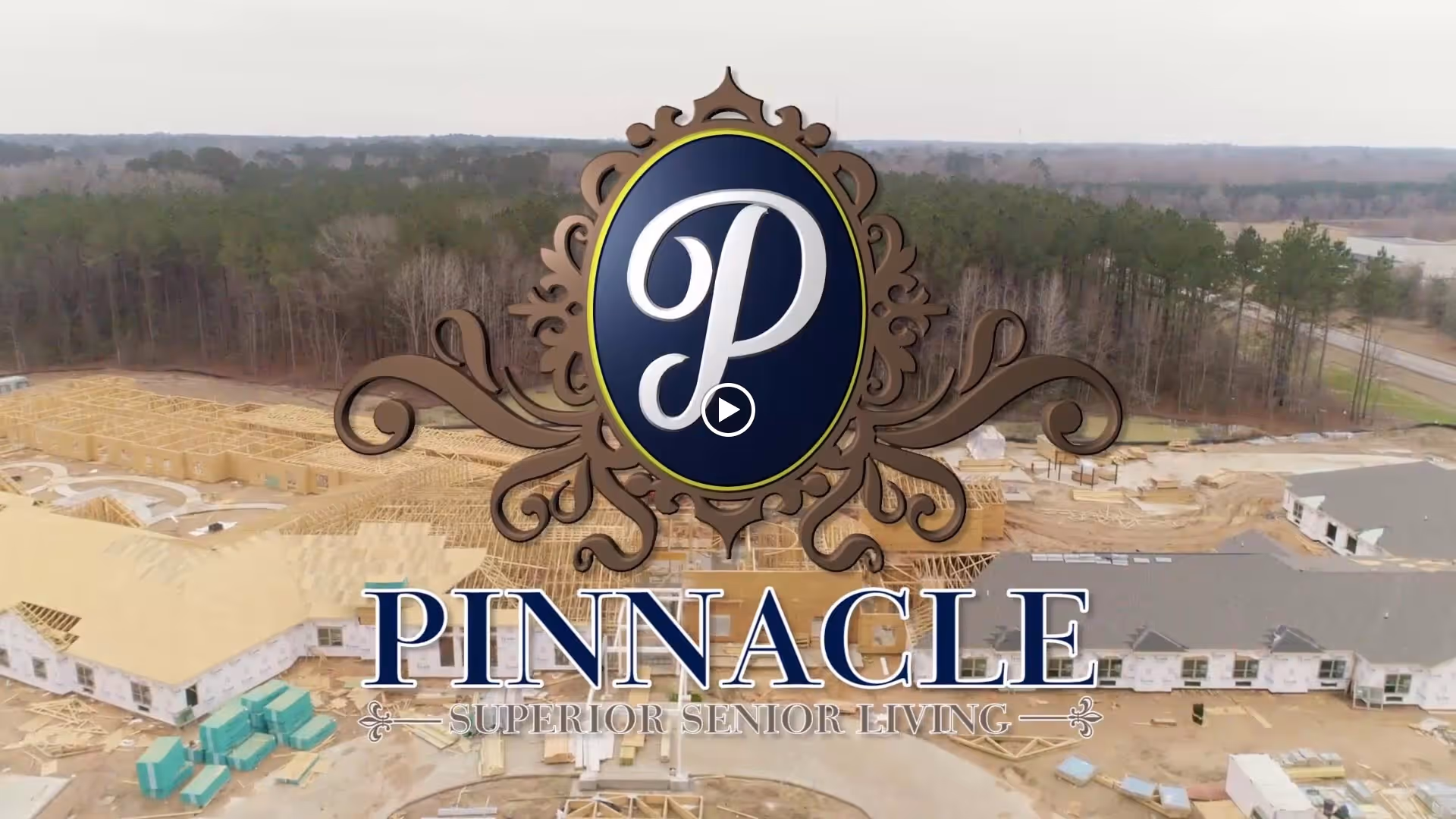 Aerial view of a senior living facility under construction surrounded by trees, with the Pinnacle Senior Living logo prominently displayed in the center.