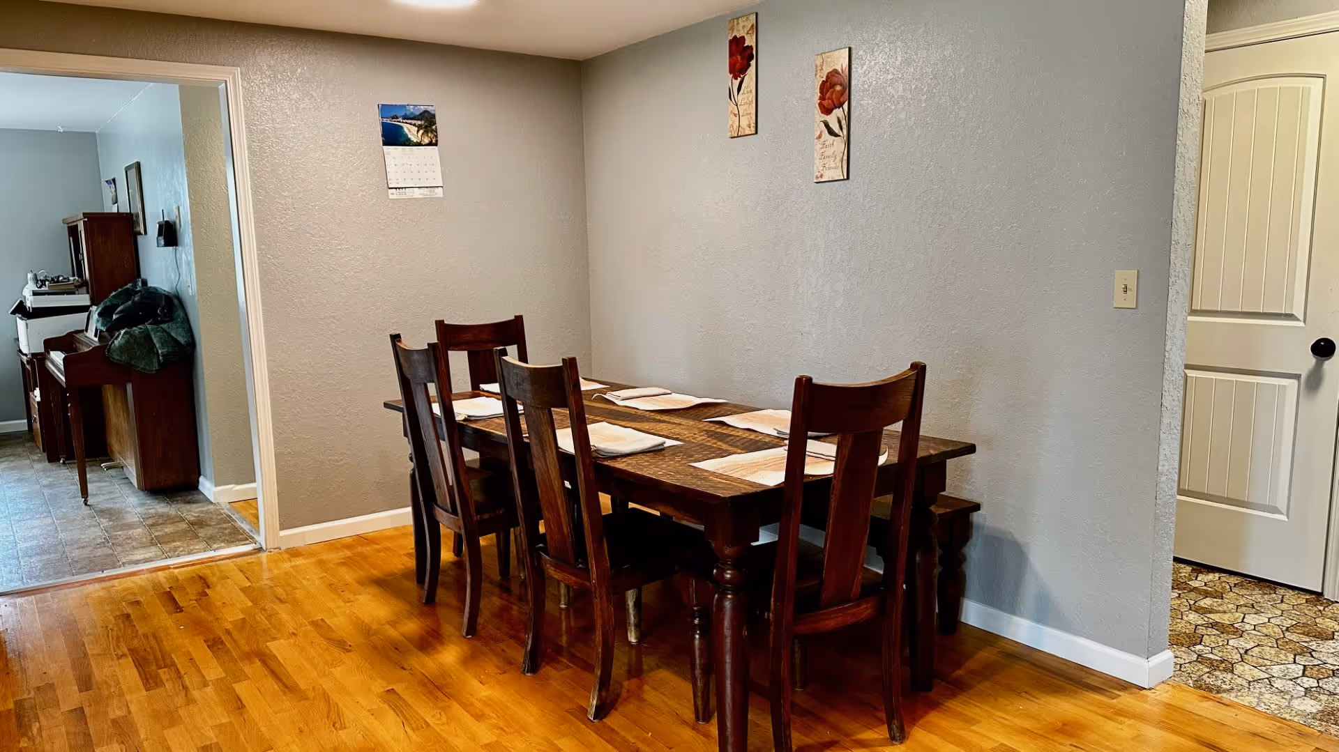 Wooden dining table with six chairs and placemats against a gray wall in a dining area.