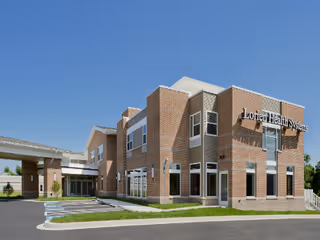 Brick senior living facility with prominent sign and glass entry under a clear blue sky.