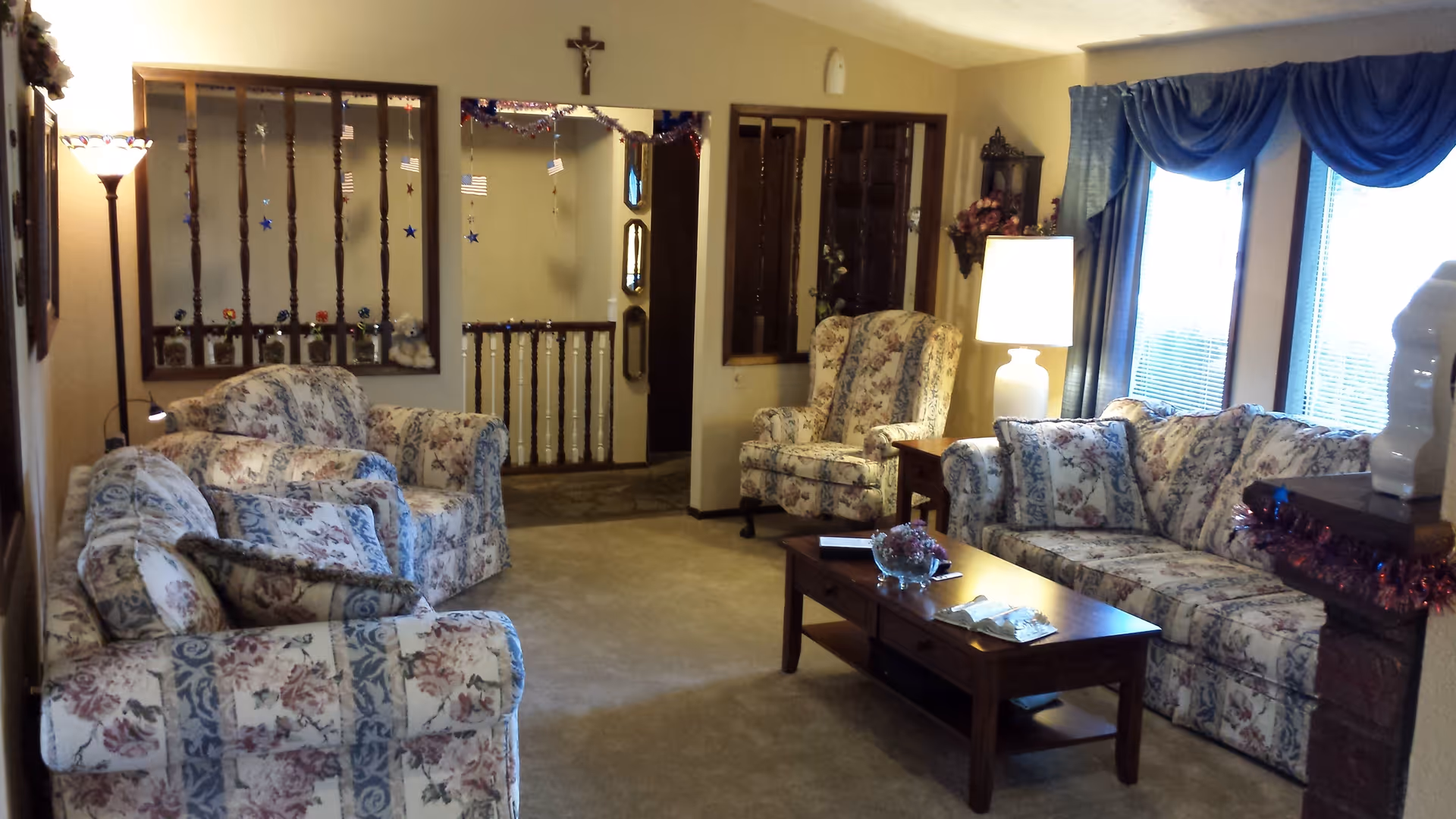 Cozy living room with matching floral sofas and armchairs, a wooden coffee table, lamps and blue-curtained windows.
