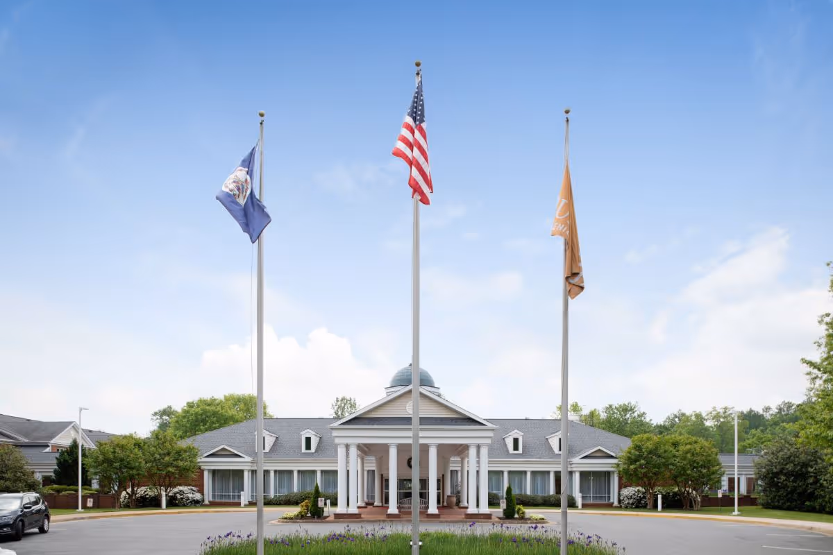 Front entrance of a senior living building with a covered portico, circular driveway, and three flagpoles.