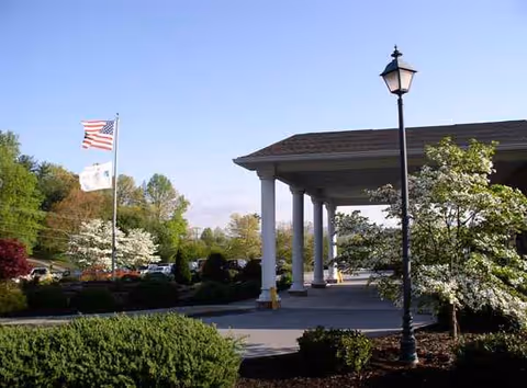 Front view of The Laurels of Hendersonville entrance with columns, flag, lamppost, and landscaping.
