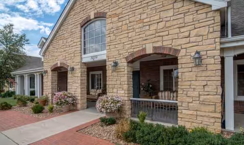 Stone facade with arched entryways, porch seating, and landscaped walkway at River Bend.