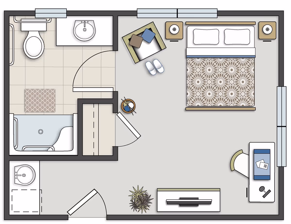 Floor plan of a senior living facility room at Alexander Guest House showing a bedroom with a bed, two nightstands, an armchair with pillows, slippers, a desk with a chair and items on it, a TV stand with a TV, a small plant, and an attached bathroom with a toilet, sink, bathtub, and a small closet area.