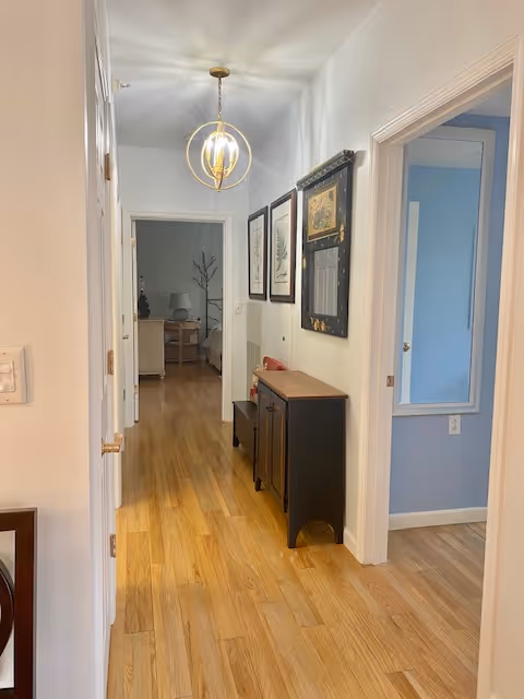 Bright interior hallway with hardwood floors, framed artwork and a console table leading to adjoining rooms.