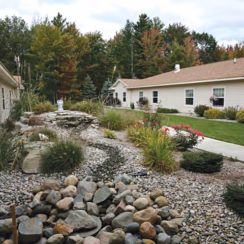 Landscaped courtyard with a rock garden and small pond between single-story beige buildings and trees in the background.