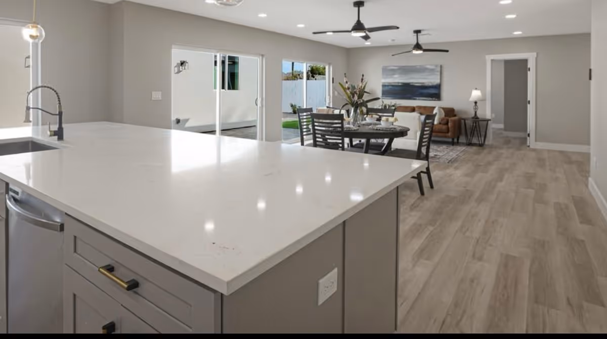 Open-plan interior showing a kitchen island in the foreground with a dining table and living area beyond.