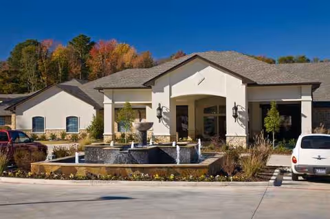 Front view of a cream-colored senior living facility with a decorative fountain.