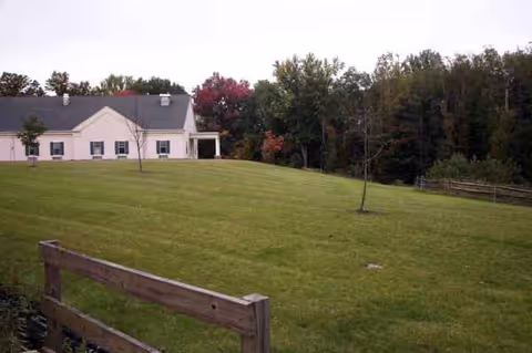 Exterior view of a care center with a large lawn, trees, and wooden fencing.