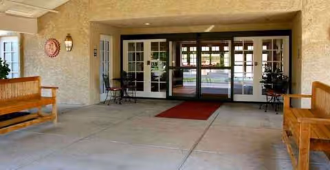 Covered entrance of Madison Meadows Retirement Community with glass doors, benches, and a red mat.