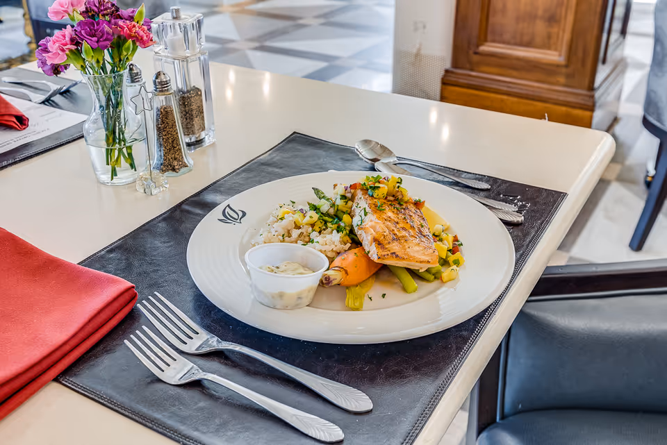 Plated salmon entrée with rice and vegetables on a placemat at a dining table with cutlery, flowers, and salt and pepper shakers.