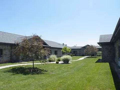 Exterior view of Manor at Elfindale senior living campus with green lawn, trees, and walkways.