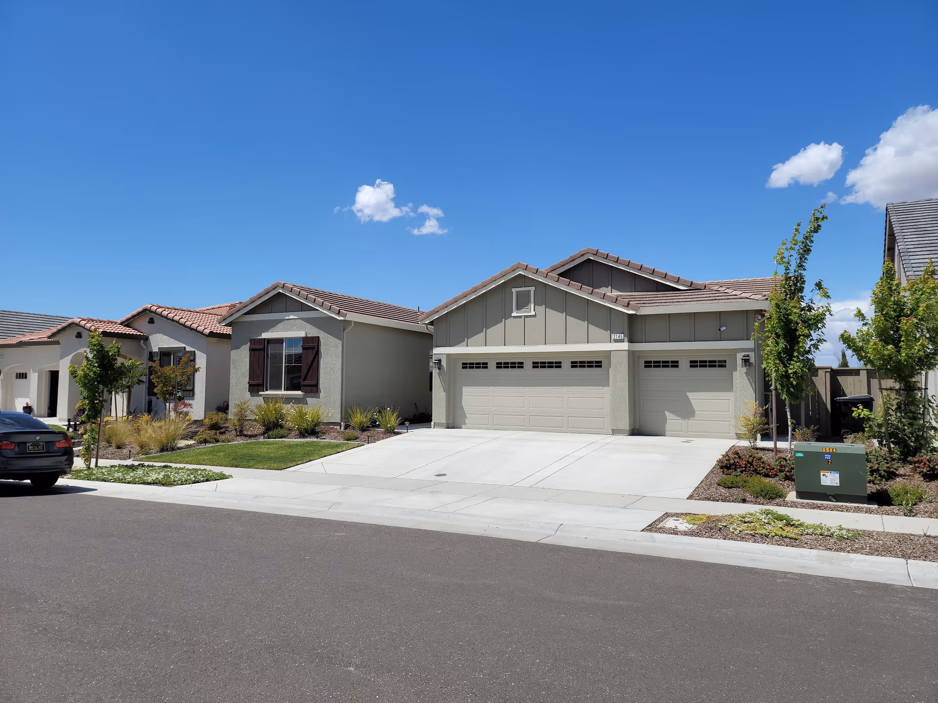 Single-story suburban house with a three-car garage and landscaped front yard under a clear blue sky.