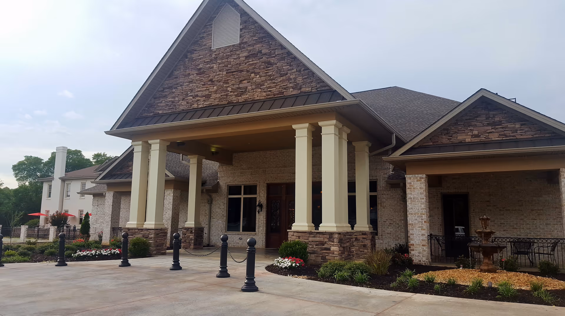 Entrance of a stone-and-brick senior living building with tall columns, a covered porte-cochère, and landscaped beds.