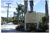 Sidewalk and landscaping with palm trees and a freestanding sign for Abbey Road Villa in front of a beige multi-story building.
