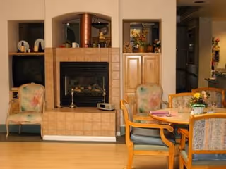 Communal seating area with a tiled fireplace, built-in cabinets, upholstered chairs, and a dining table.