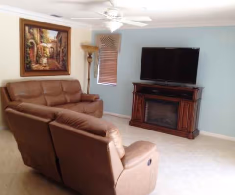A living room in a senior facility with brown leather seating, a TV stand, and fireplace.