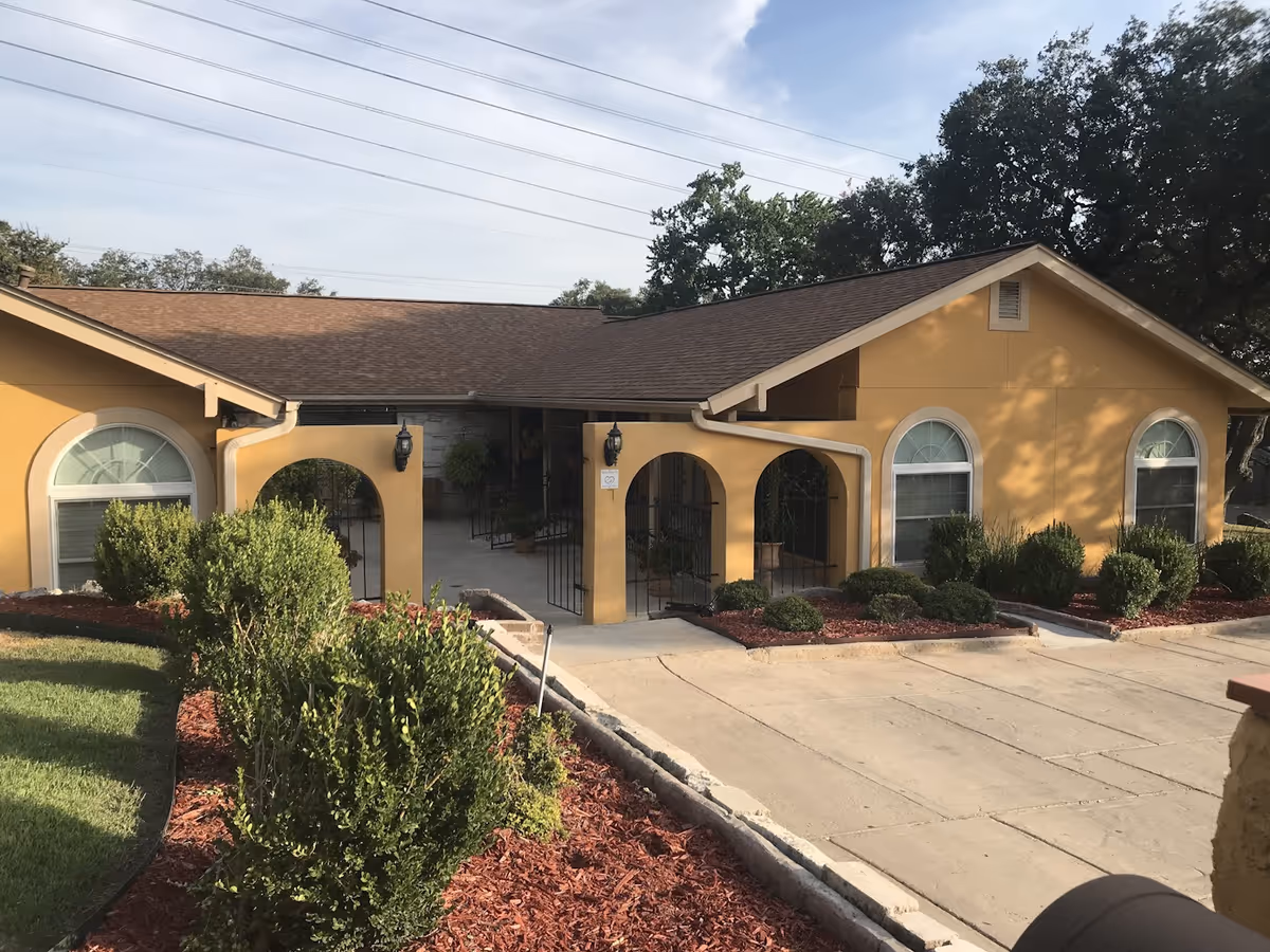 Yellow, single-story senior facility exterior with arched windows and landscaped entry.