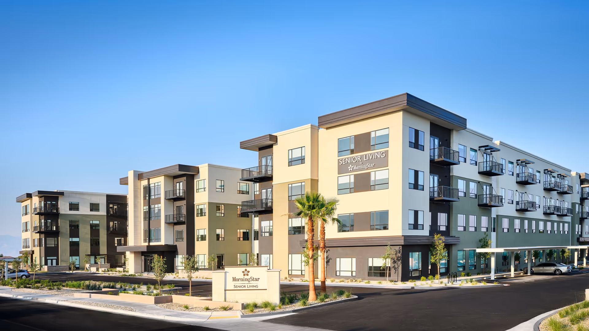 Exterior view of the MorningStar at The Canyons senior living building with balconies, landscaping, and a front sign under a clear blue sky.