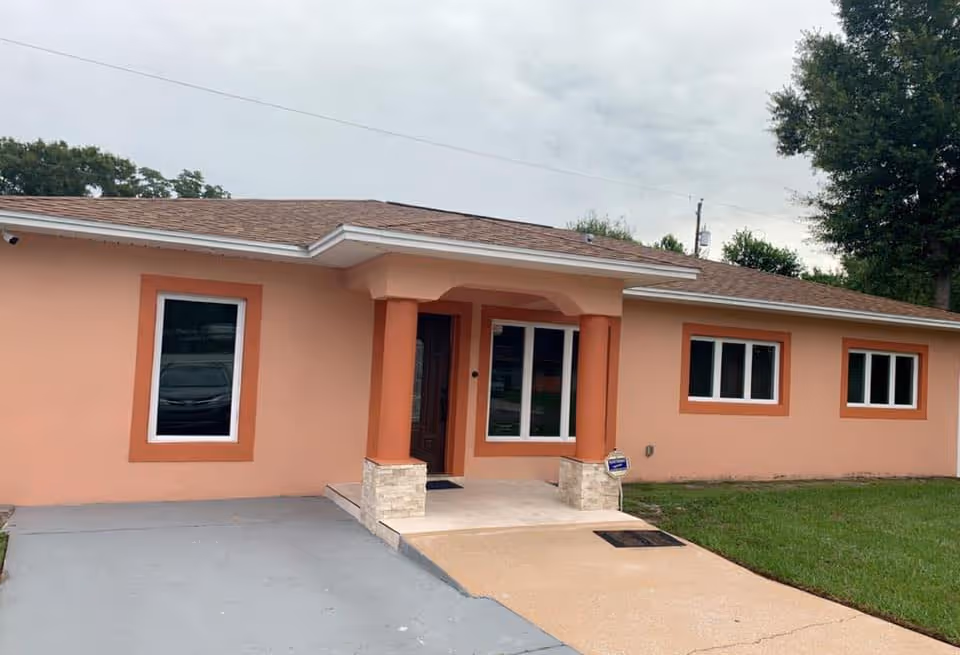 Single-story peach-colored building front with a covered entrance supported by columns, multiple windows, lawn, and a driveway.
