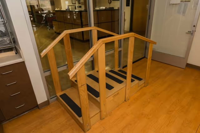 Small wooden practice staircase with handrails on a wood floor inside a rehabilitation facility.