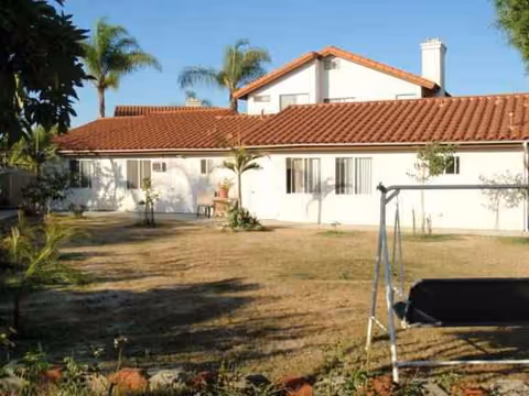 White single-story building with red tile roof, palm trees, and a swing in the yard.