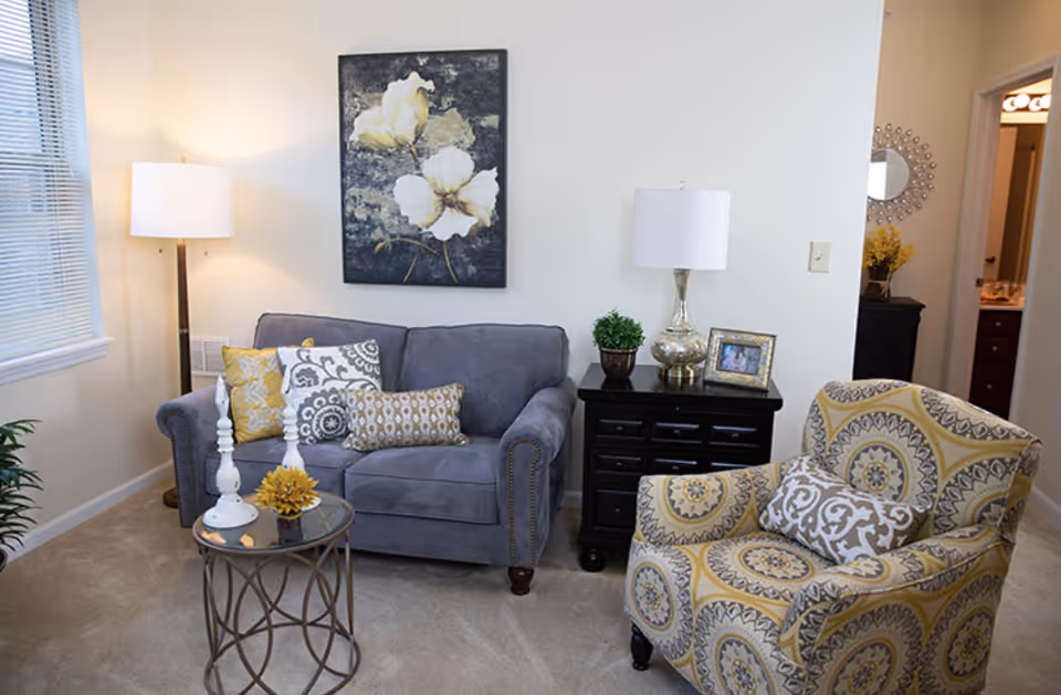 Cozy living room with a gray loveseat, patterned armchair, side tables with lamps, and floral wall art.