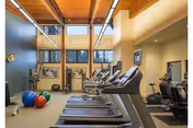 Fitness center with treadmills, weight machines, exercise balls and large windows beneath a wood-beamed ceiling.