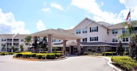 Senior living facility exterior with porte-cochere, landscaping, and a circular driveway.