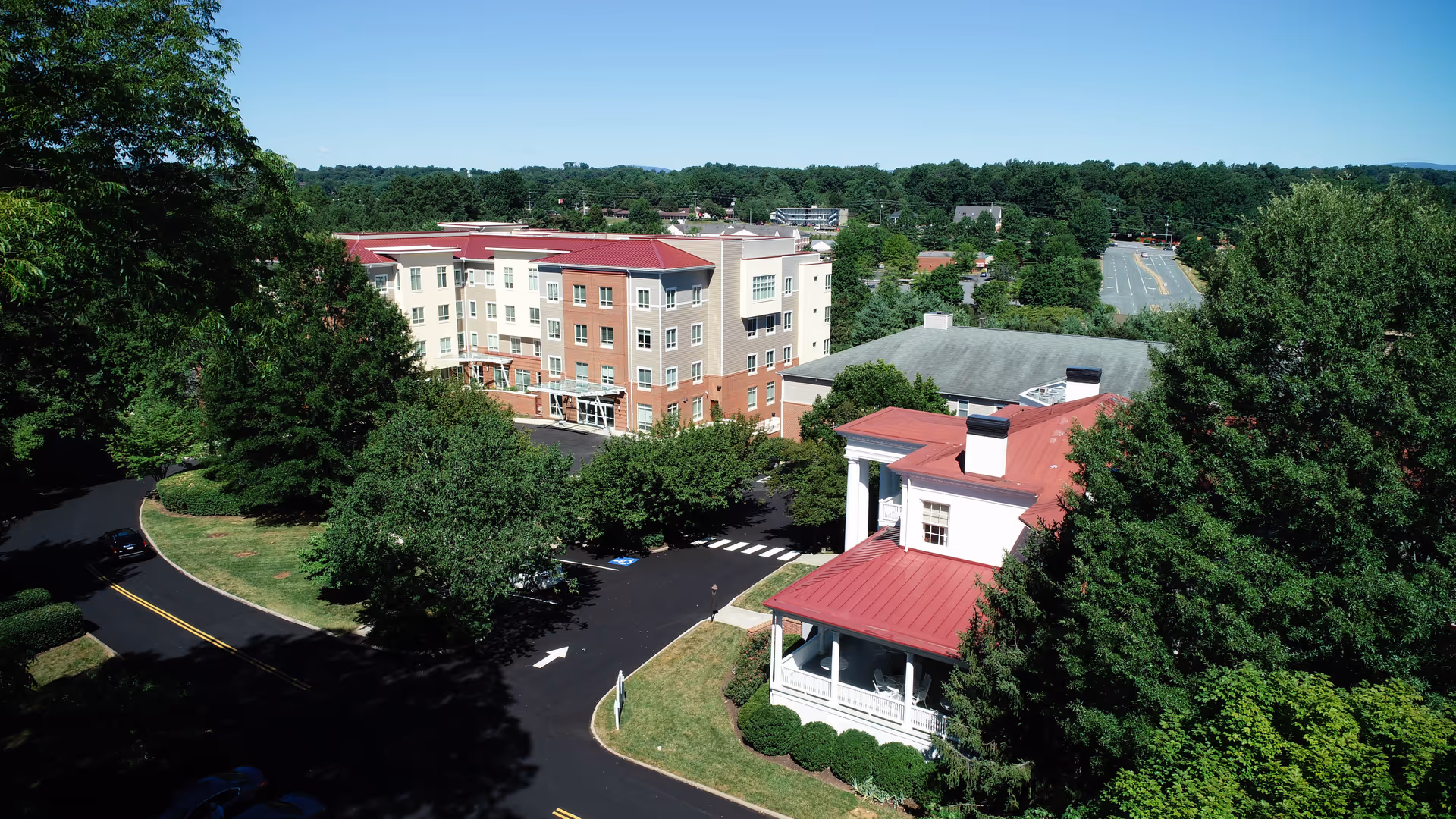 Aerial view of an assisted living campus featuring multi-story and red-roofed buildings surrounded by trees and a curved driveway.