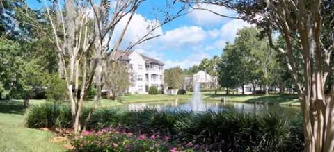 Scenic outdoor view of a pond with fountain, trees, and buildings in Brookdale Southside grounds.