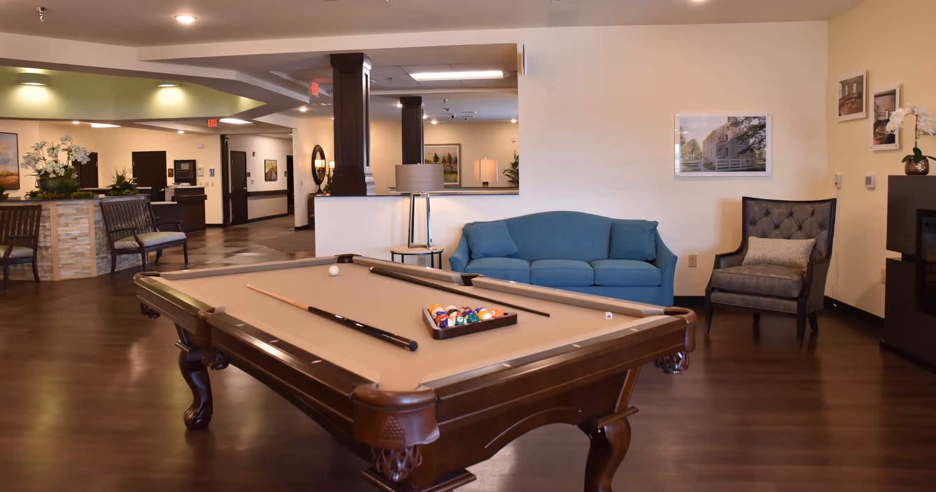 Communal lounge with a pool table in the foreground, blue sofa and armchair seating, and a reception area in the background.