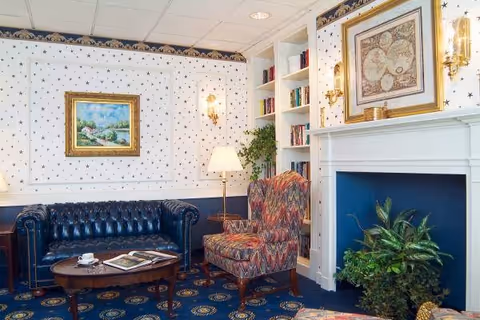 Cozy sitting room with a tufted leather sofa, patterned armchairs, a coffee table, built-in bookshelves, and a decorative fireplace.