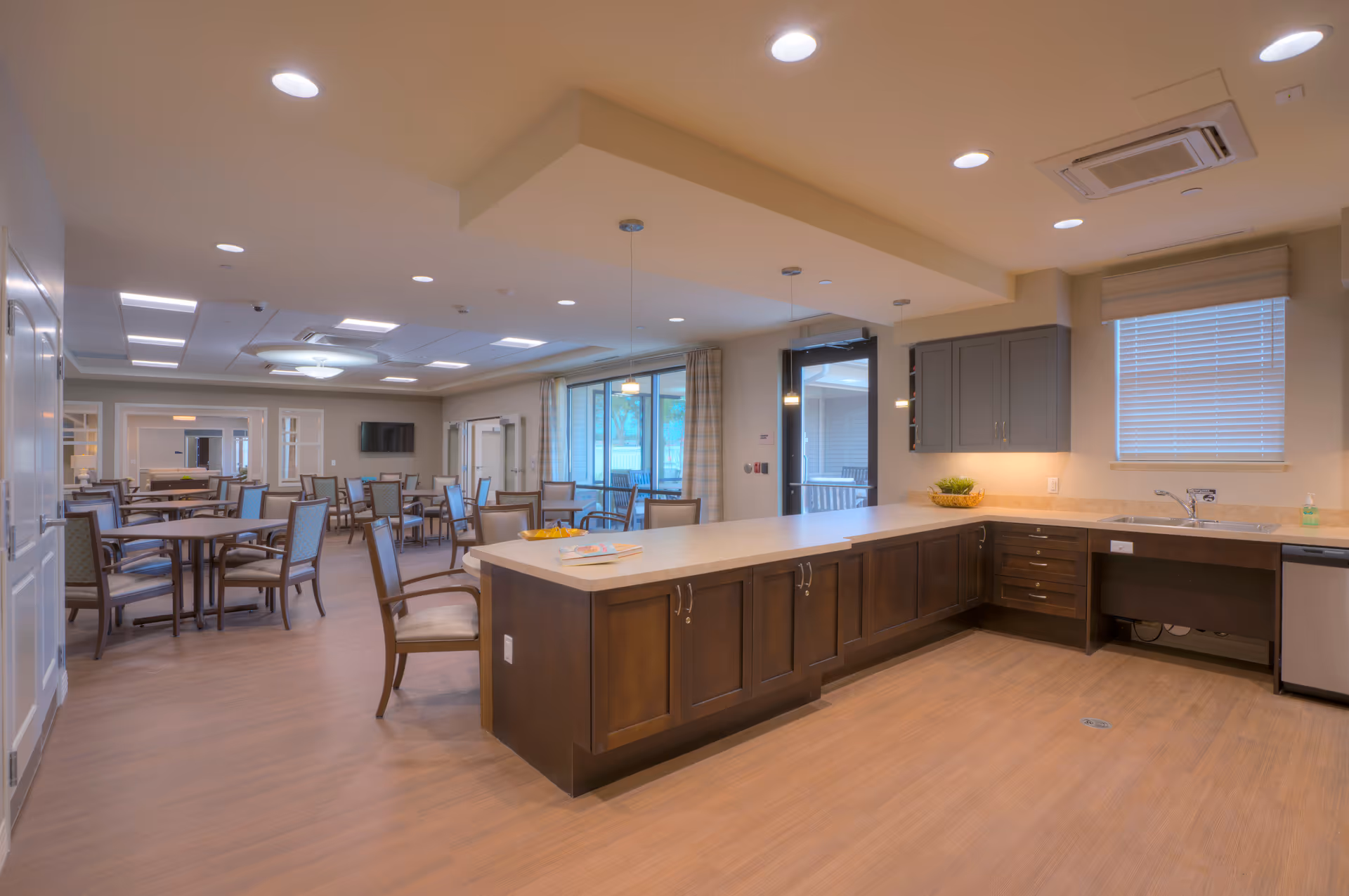 Open communal dining area with multiple tables and chairs and a large kitchen island/counter in the foreground.