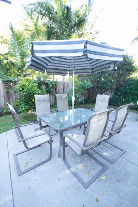 Outdoor patio with glass table, six chairs, and striped umbrella.