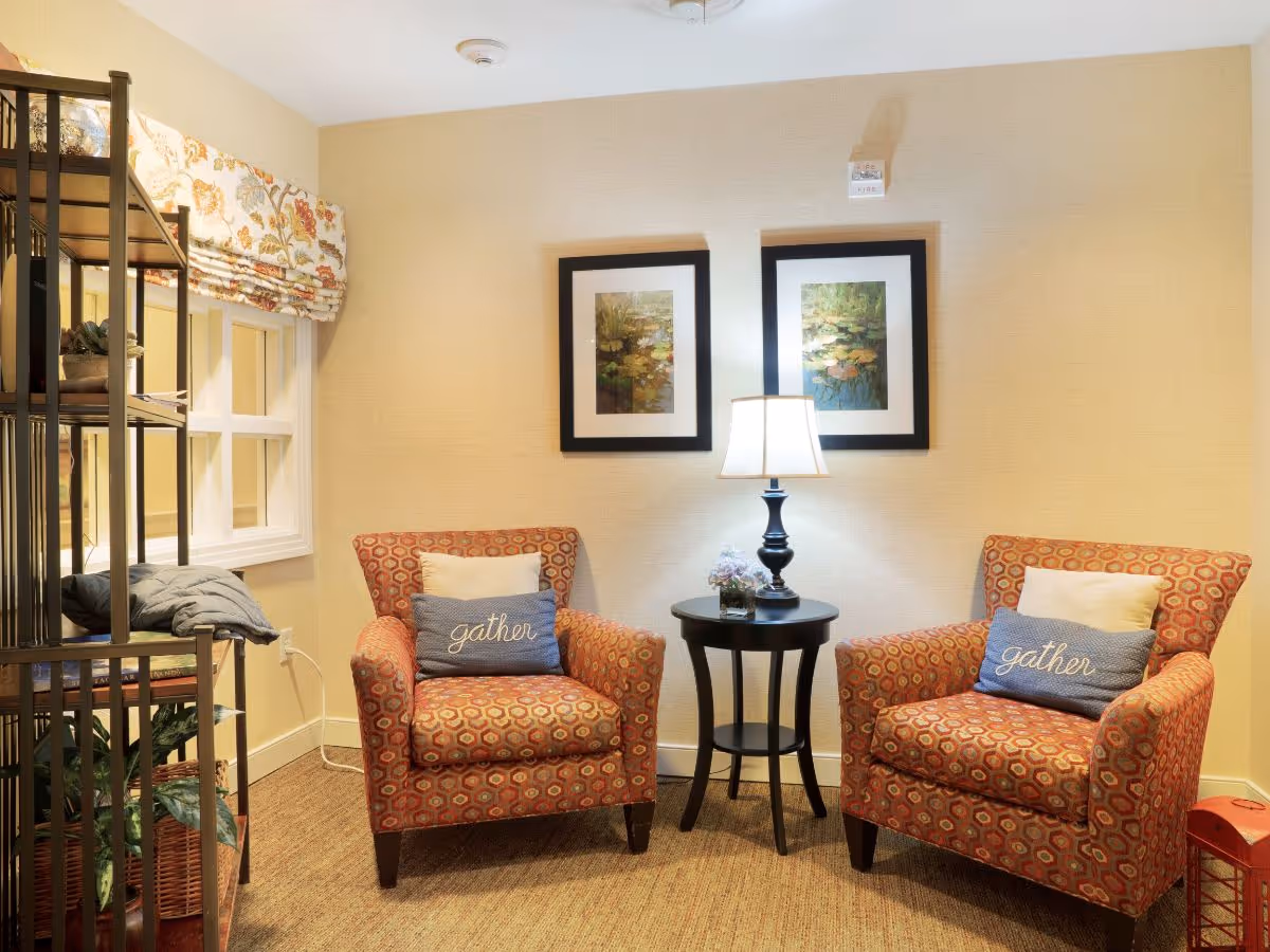 Two patterned armchairs with 'gather' pillows flank a small round table and lamp in a cozy sitting area.