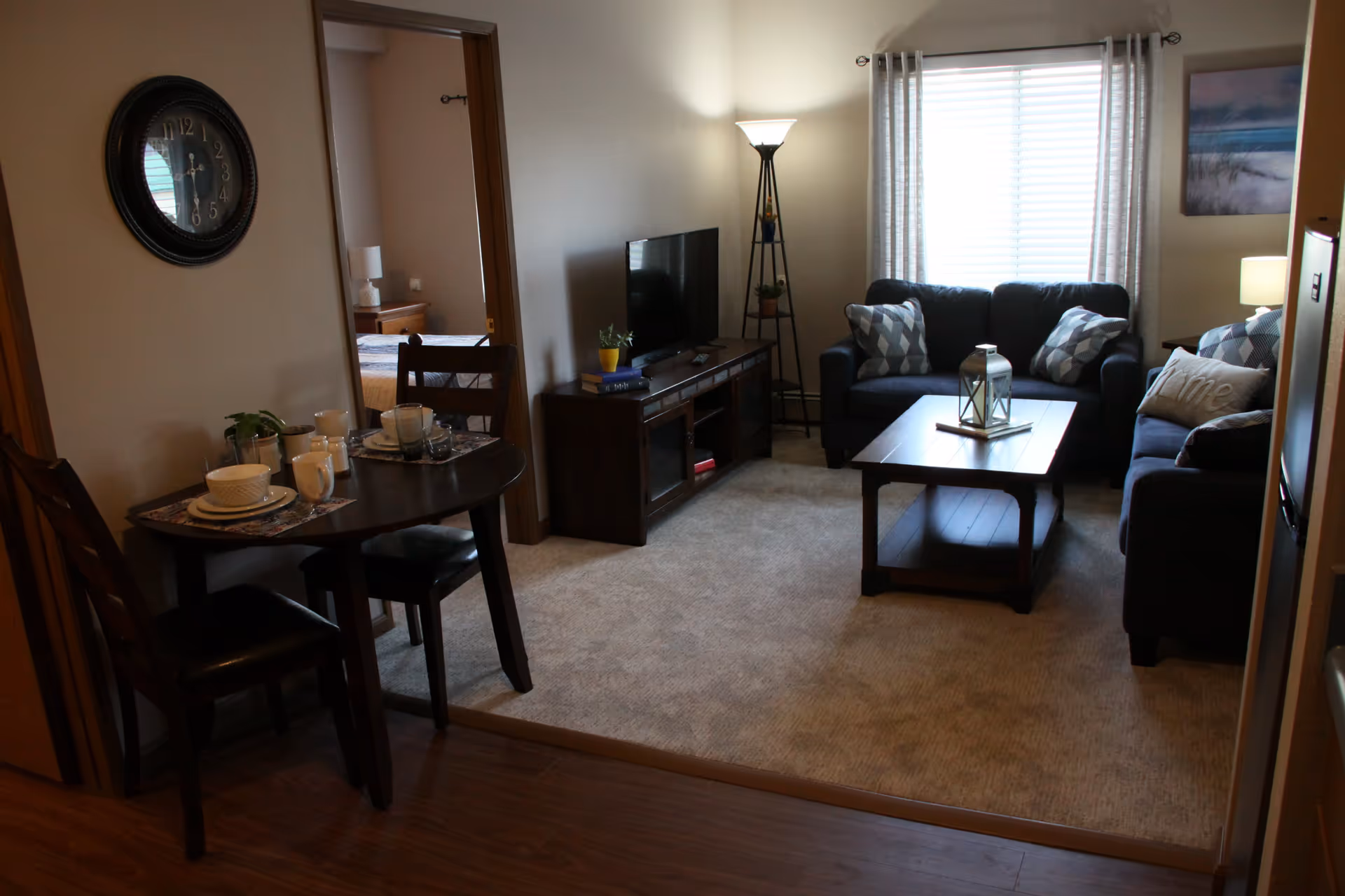 Cozy furnished living room with two sofas, a coffee table, TV stand and a small dining table near an open doorway to a bedroom.