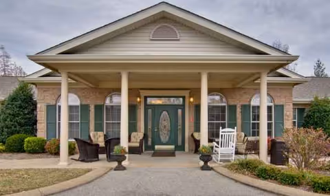 Front entrance of Alexandria Place, a brick senior living facility with a covered porch and chairs.