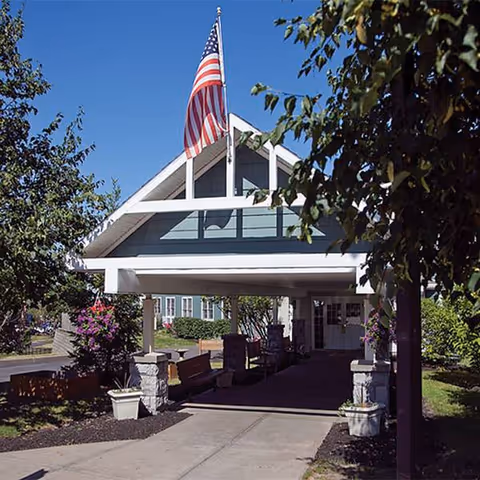 Front entrance of a senior living facility with flag and covered walkway.