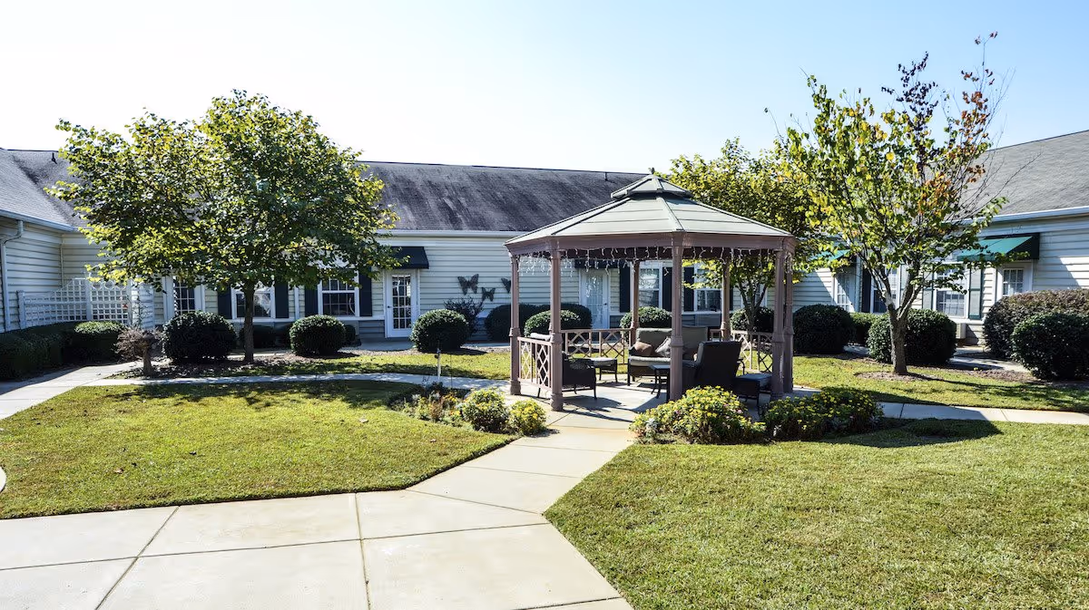 A gazebo with outdoor seating in a grassy courtyard surrounded by single-story senior living buildings and paved walkways.