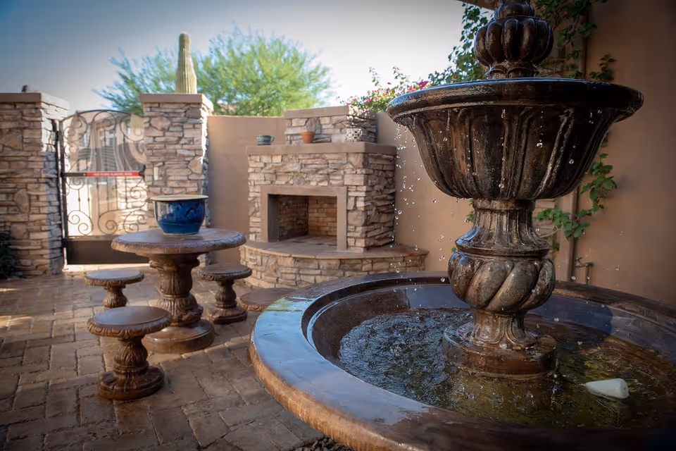 Stone courtyard patio featuring a tiered fountain, round stone table with stools, and a built-in stone fireplace.
