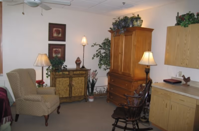 Cozy living room with an upholstered armchair, wooden cabinets and armoire, lamps, wall art, and a rocking chair.
