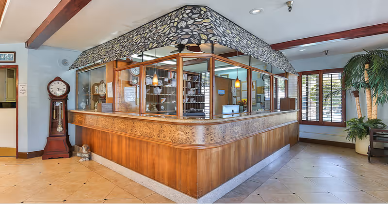 Interior lobby with curved wooden reception desk, glass partitions, a grandfather clock, and plants.