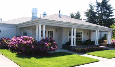 A single-story senior living facility with a covered front porch and flowering bushes.