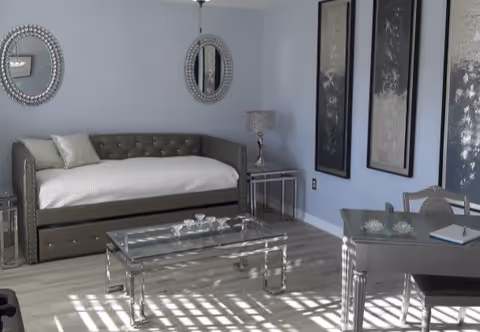 Light-filled living room with a daybed, glass coffee table, mirrored accents, desk, and wall decor.