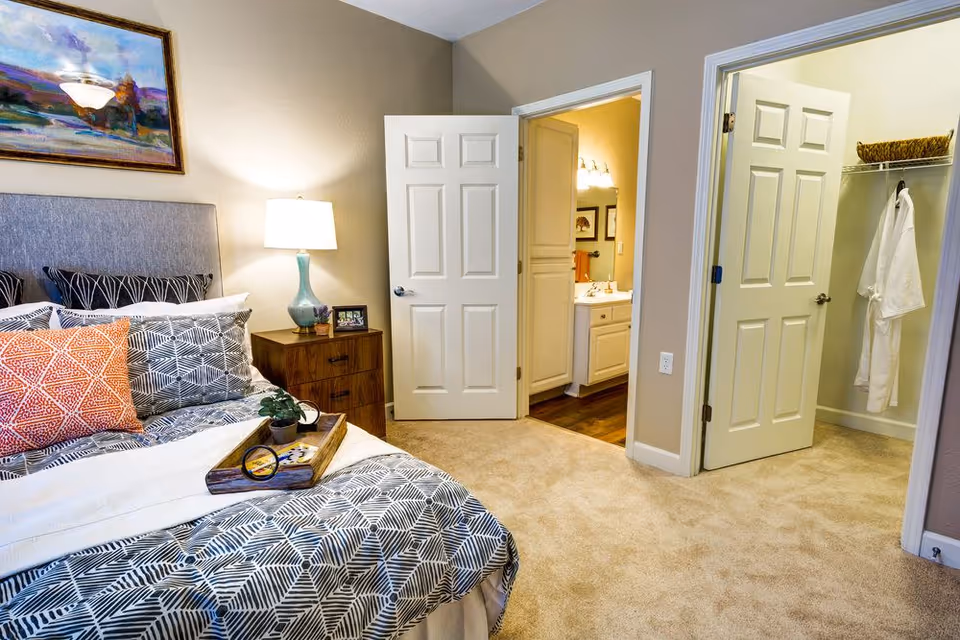 Well-decorated bedroom with a bed, nightstand and open doors leading to a bathroom and walk-in closet.