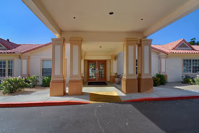 Covered porte-cochère entrance with columns and double glass doors leading into a single-story building.