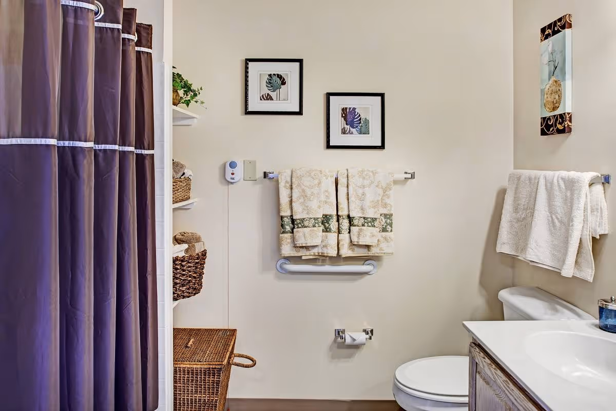 Bathroom with a purple shower curtain, toilet and sink, towel racks with folded towels, framed wall art, and woven storage baskets.