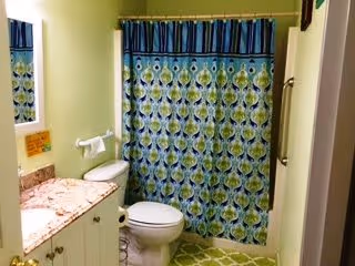 Small bathroom with a blue-and-green patterned shower curtain, toilet, vanity with sink and mirror, and pale green walls.