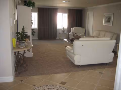 Bright living room with white leather sofas, tiled entry, and potted plants.